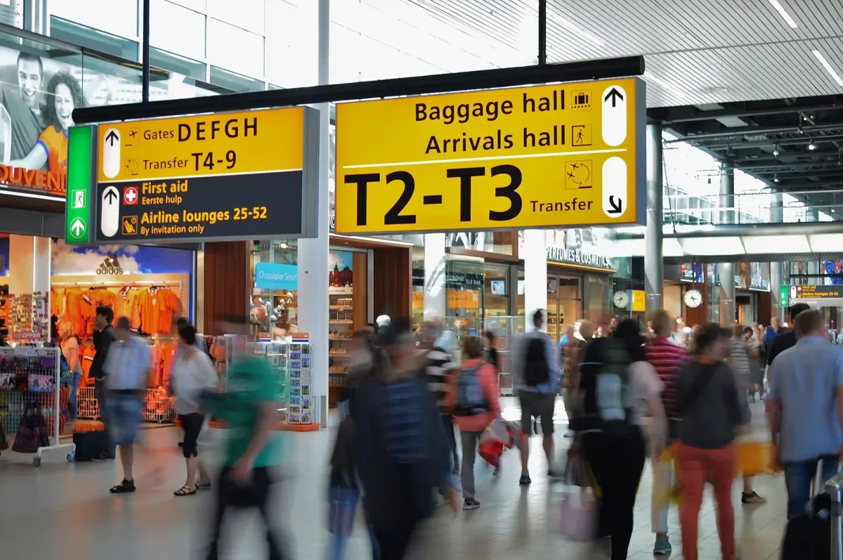 Reizigers in een luchthavenhal onder de gele borden voor aankomst en bagage
