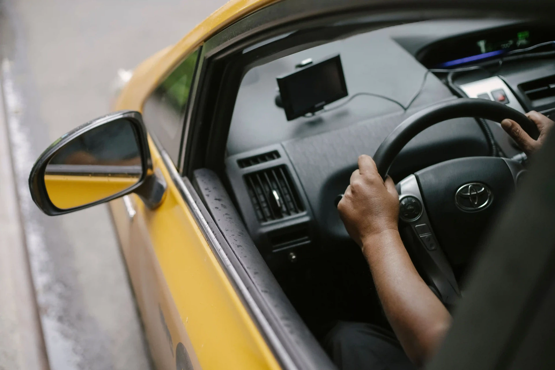 Handen van een taxichauffeur aan het stuur, gezien door het zijraam