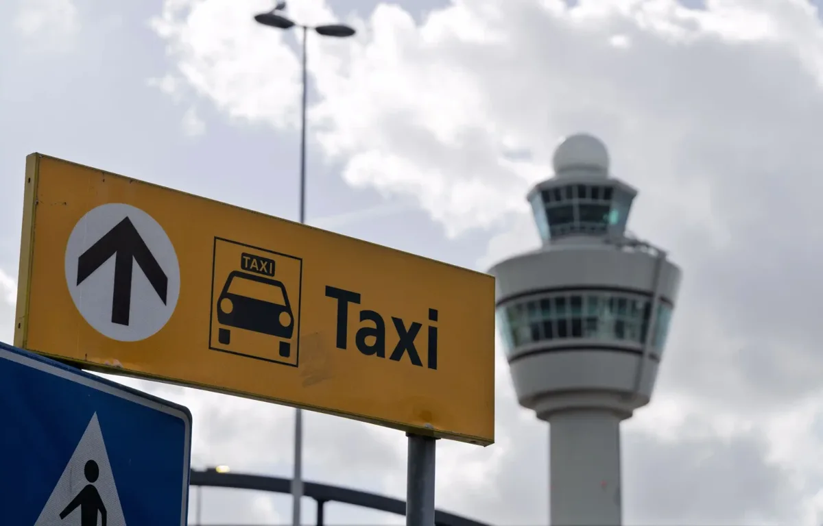 Geel bord richting de taxistandplaats met een verkeerstoren op de achtergrond