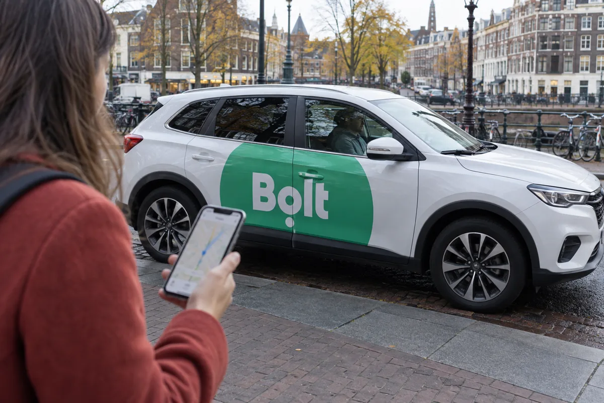 Passagier met smartphone naast een witte Bolt-taxi in een stadsstraat