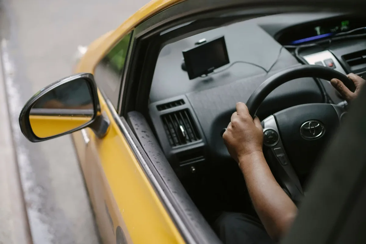 Bestuurder met een hand aan het stuur, gezien door de open zijdeur van een auto