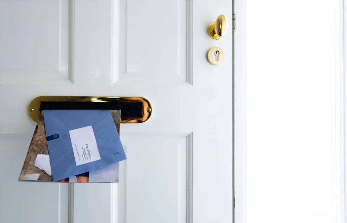 Blauwe envelop van de Belastingdienst steekt door de brievenbus van een witte voordeur